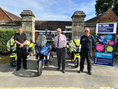 Three people stand between motorcycles