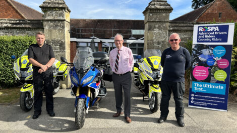 Three people stand between motorcycles