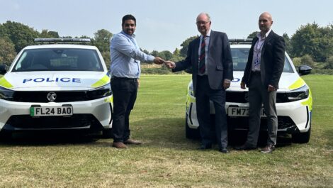 Three people stand in front of a line of police cars.